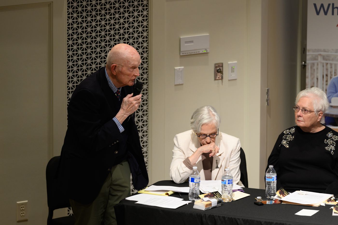 A debater stands with a microphone to question the other team while teammates listen.